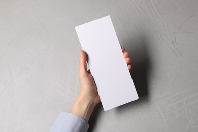Woman holding blank card at light grey table, top view. Mockup for design