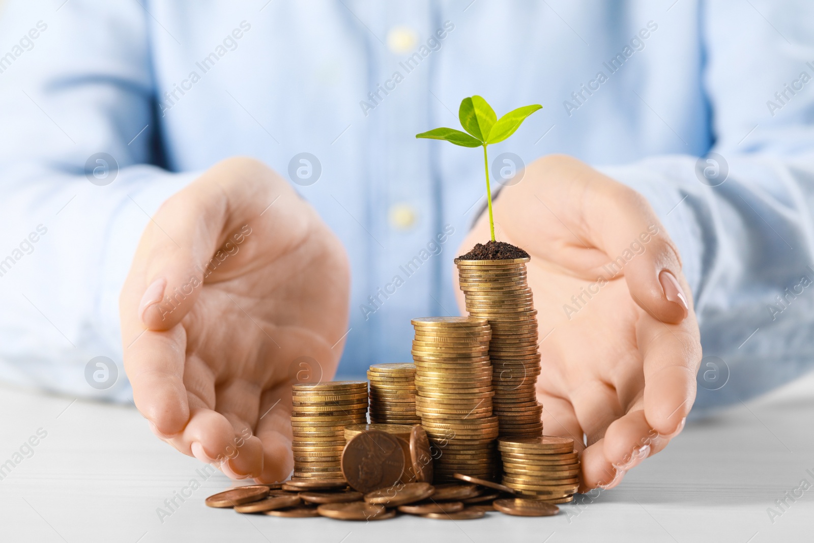 Photo of Woman with stack of coins and green sprout at white table, closeup. Investment concept