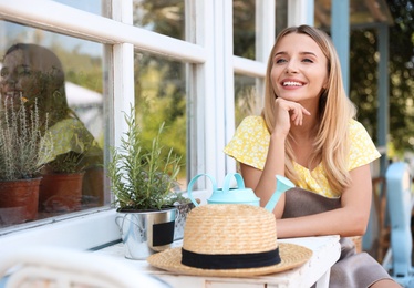 Photo of Young woman with home plant sitting at white wooden table outdoors