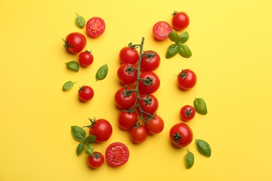 Fresh cherry tomatoes and basil leaves on yellow background, flat lay