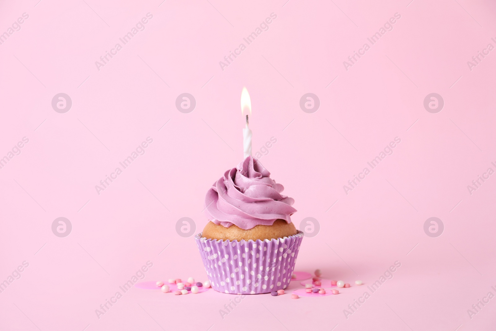Photo of Delicious birthday cupcake with burning candle and sprinkles on pink background