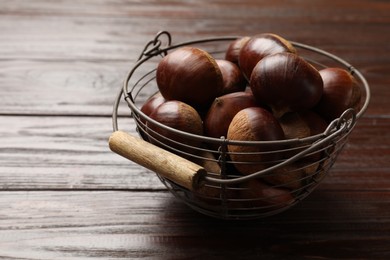 Photo of Sweet fresh edible chestnuts in metal basket on wooden table, closeup. Space for text