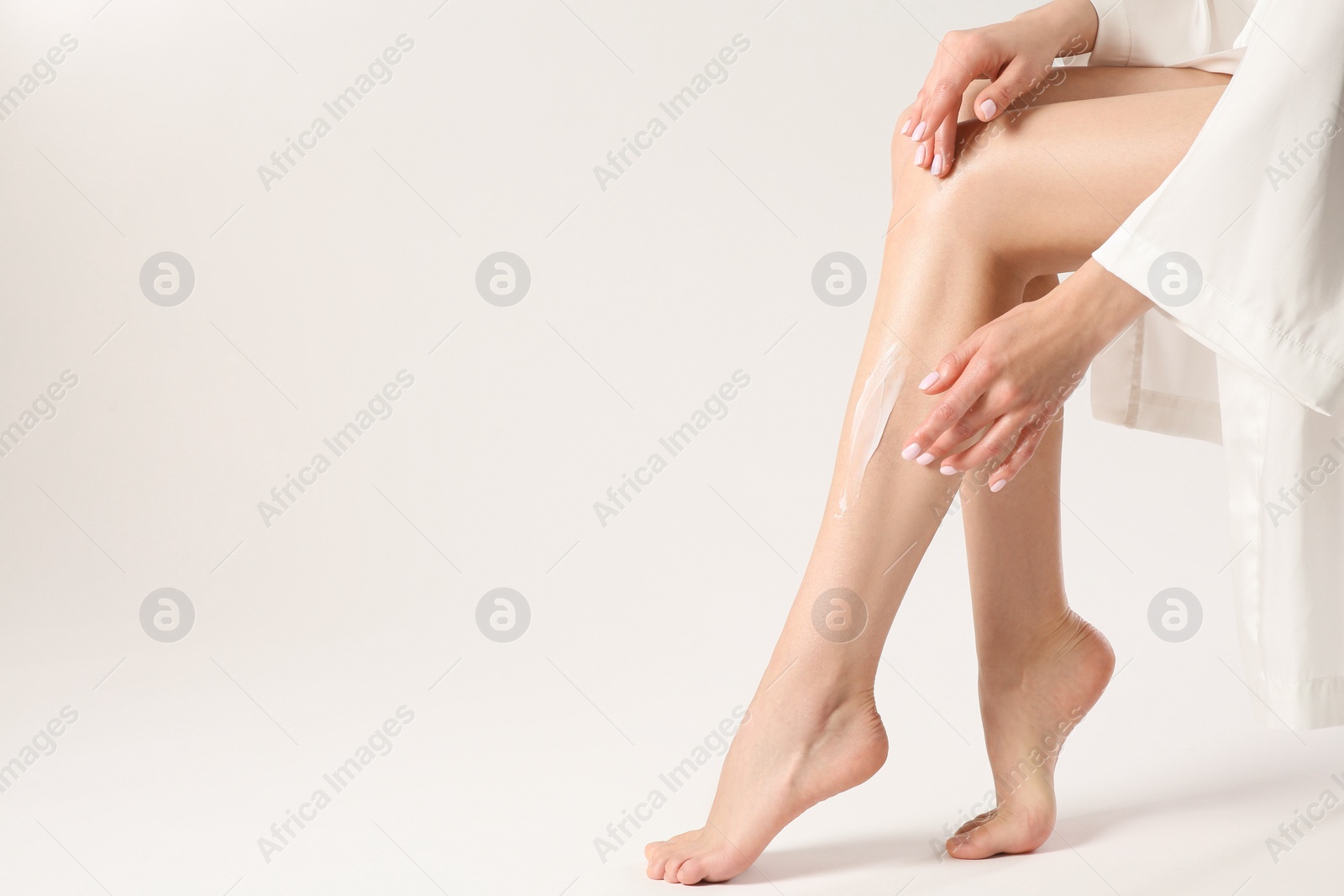 Photo of Woman applying body cream onto her smooth legs on white background, closeup. Space for text