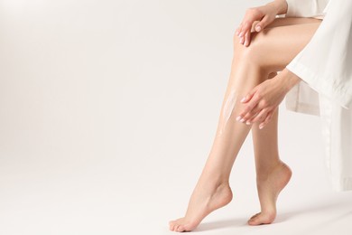 Photo of Woman applying body cream onto her smooth legs on white background, closeup. Space for text