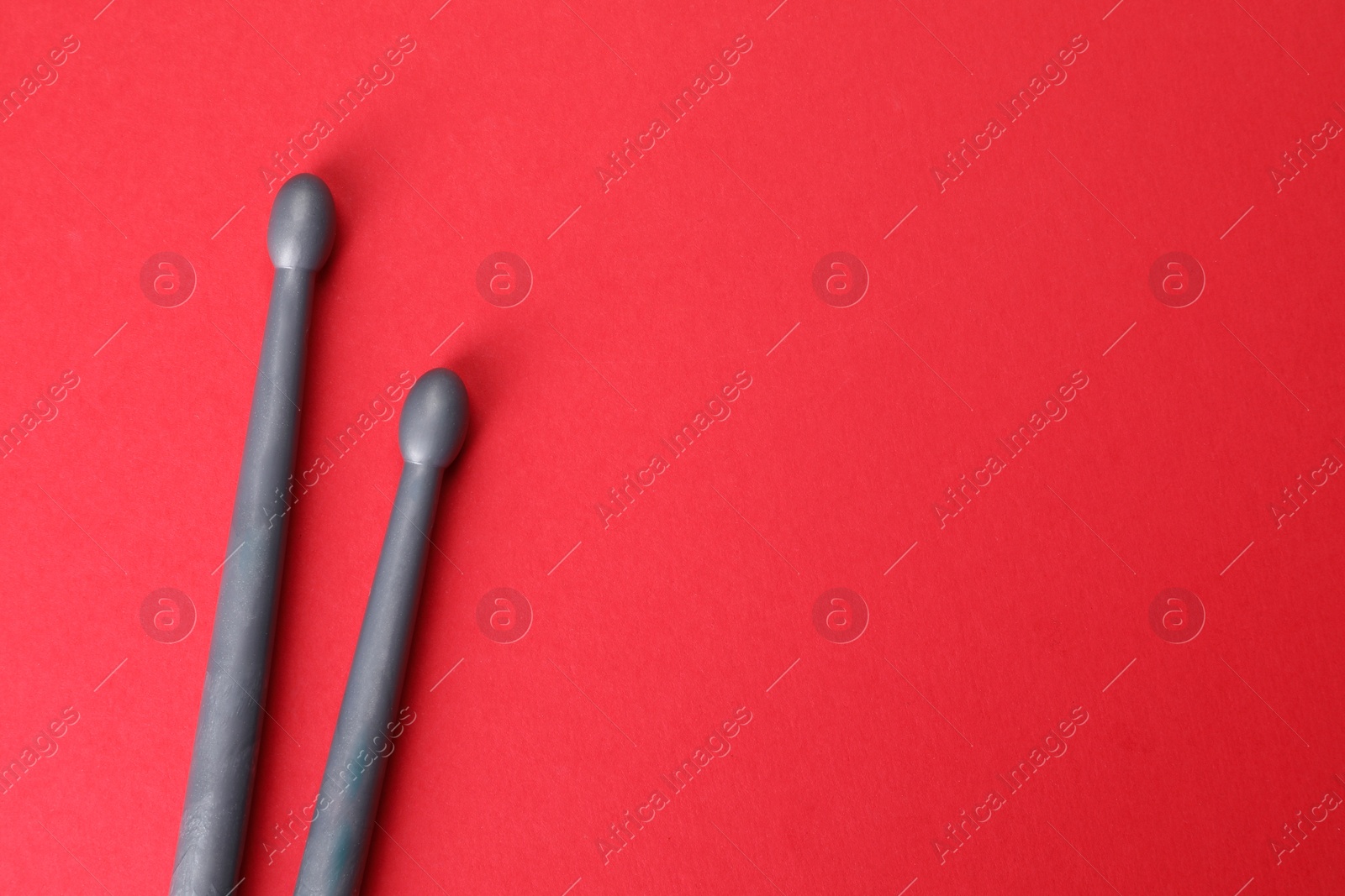 Photo of Two gray drum sticks on red background, top view. Space for text