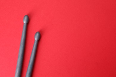 Two gray drum sticks on red background, top view. Space for text