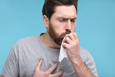 Sick man with tissue coughing on light blue background