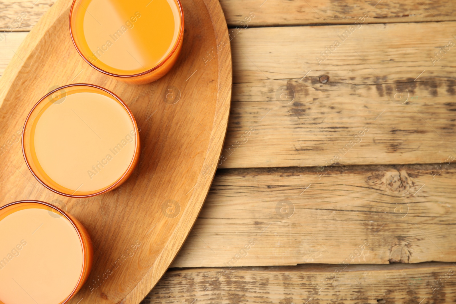 Photo of Glasses of freshly made carrot juice on wooden plate, top view. Space for text