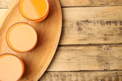 Glasses of freshly made carrot juice on wooden plate, top view. Space for text