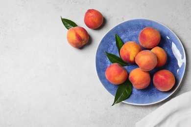Photo of Many whole fresh ripe peaches and green leaves in plate on white table, flat lay. Space for text