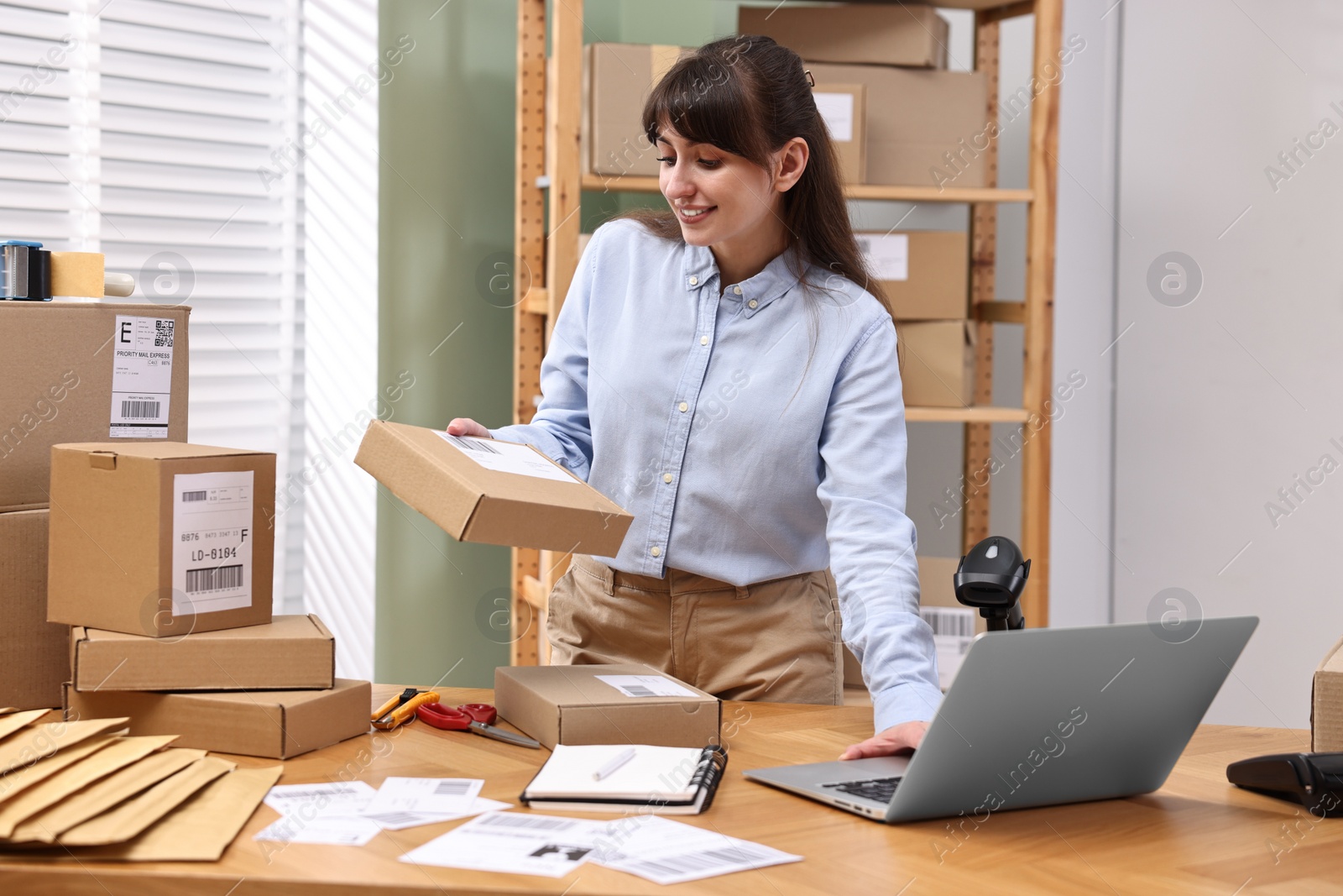 Photo of Parcel packing. Post office worker using laptop at wooden table indoors