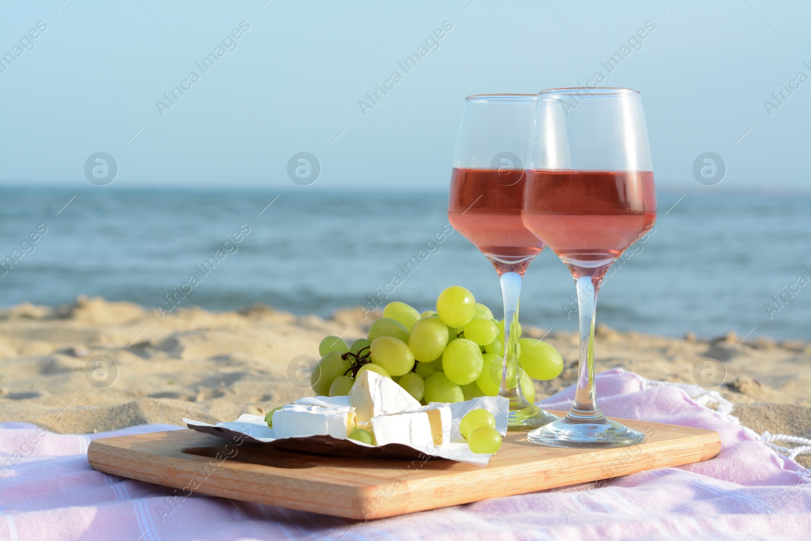 Photo of Glasses with rose wine and snacks on sandy seashore. Space for text