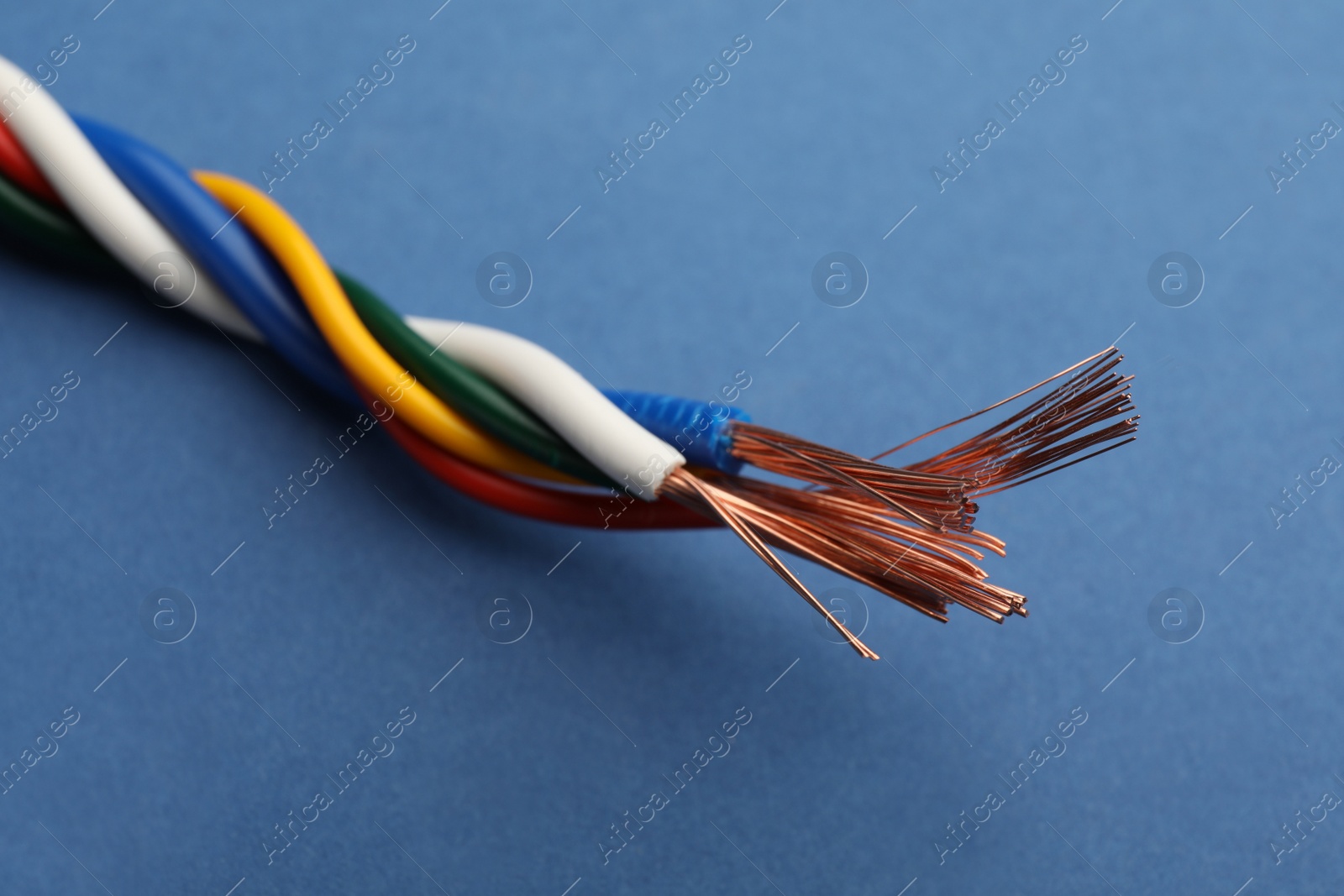 Photo of Many twisted electrical wires on blue background, closeup