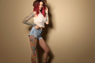 Photo of Beautiful woman with tattoos on body against beige background