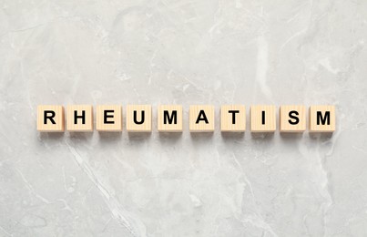 Photo of Word Rheumatism made of cubes on light gray marble table, top view