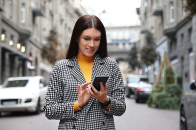 Photo of Beautiful woman in stylish suit using smartphone on city street