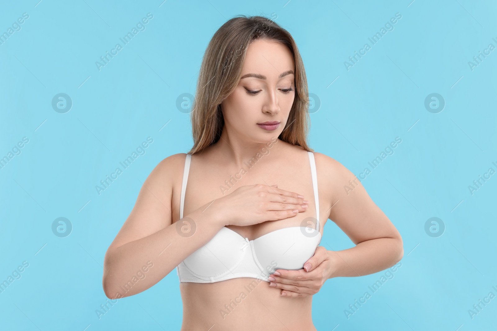 Photo of Mammology. Young woman doing breast self-examination on light blue background