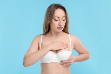 Mammology. Young woman doing breast self-examination on light blue background