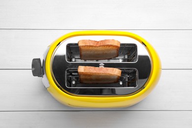 Photo of Yellow toaster with roasted bread on white wooden table, top view