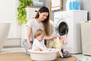 Photo of Happy mother with her daughter having fun while washing baby clothes in bathroom