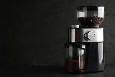 Modern electric coffee grinder on black table. Space for text