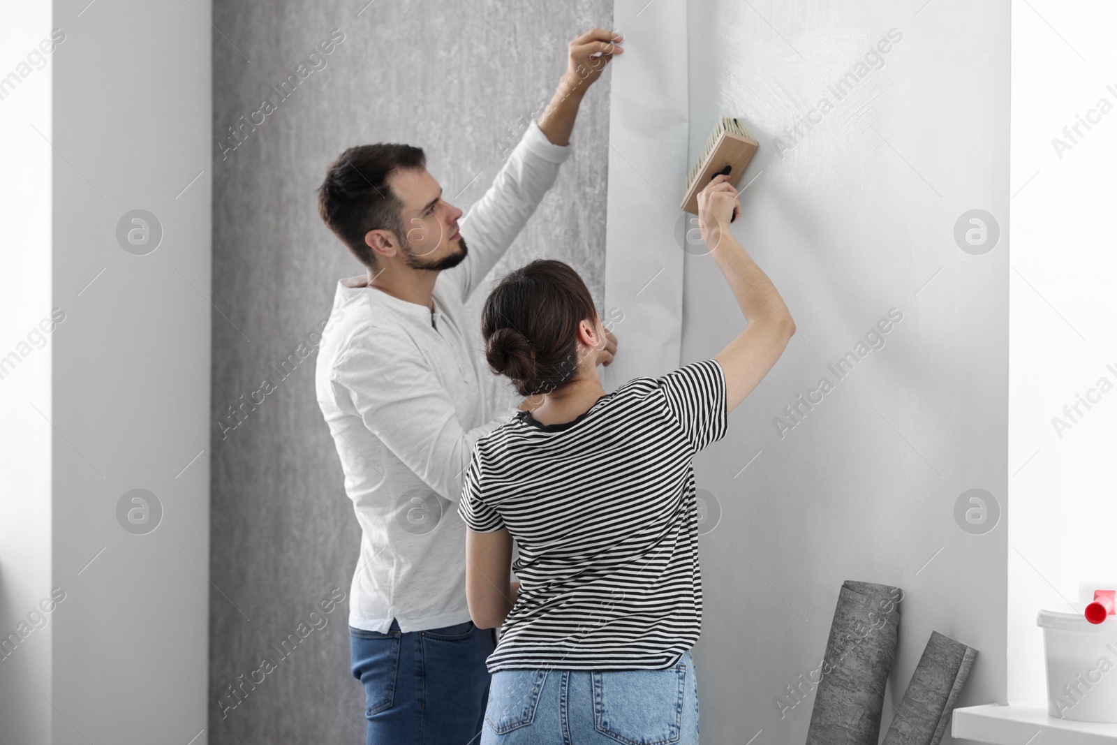 Photo of Woman and man hanging gray wallpaper in room