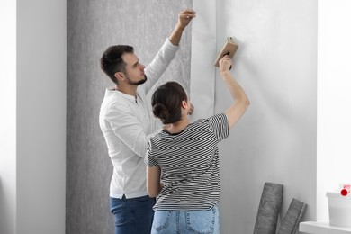Woman and man hanging gray wallpaper in room