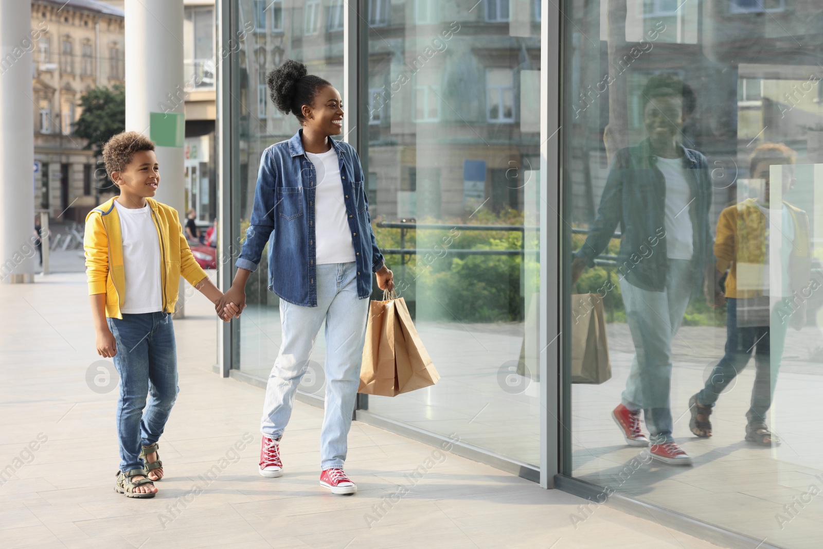 Photo of Family shopping. Happy mother and son with purchases near mall outdoors