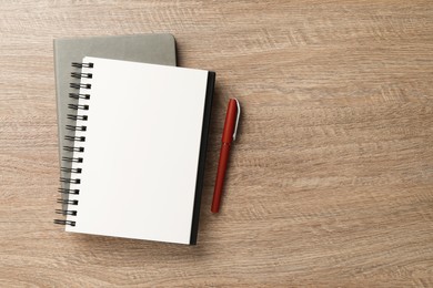 Photo of Notebooks and pen on wooden table, flat lay. Space for text