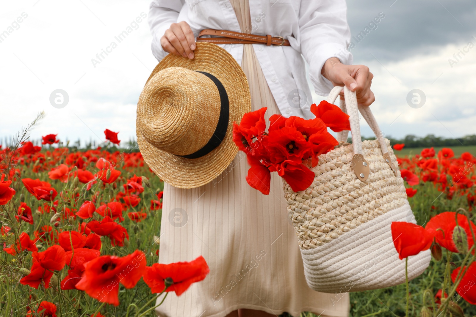 Photo of Woman holding straw hat and handbag with poppy flowers in beautiful field, closeup