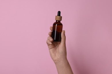 Photo of Woman holding bottle of cosmetic product on pink background, closeup