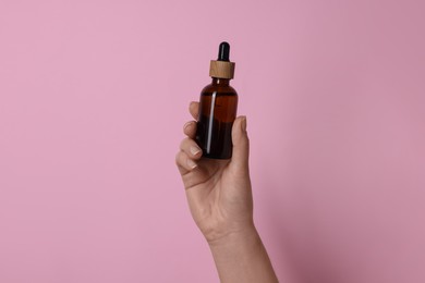 Woman holding bottle of cosmetic product on pink background, closeup