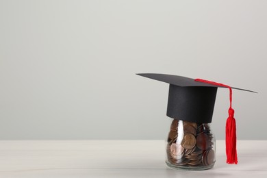Photo of Scholarship concept. Graduation cap and coins on white wooden table, space for text
