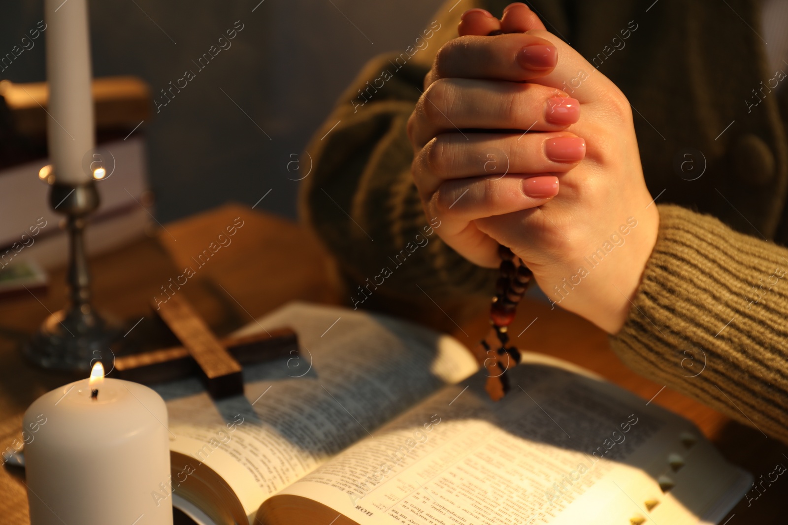 Photo of Woman praying at table with burning candle and Bible, closeup