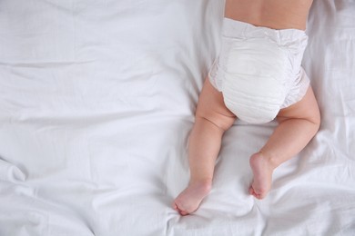 Photo of Top view of cute baby in dry soft diaper on white bed. Space for text