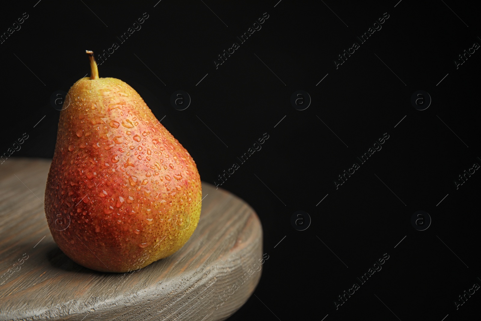 Photo of Ripe juicy pear on brown wooden table against black background. Space for text