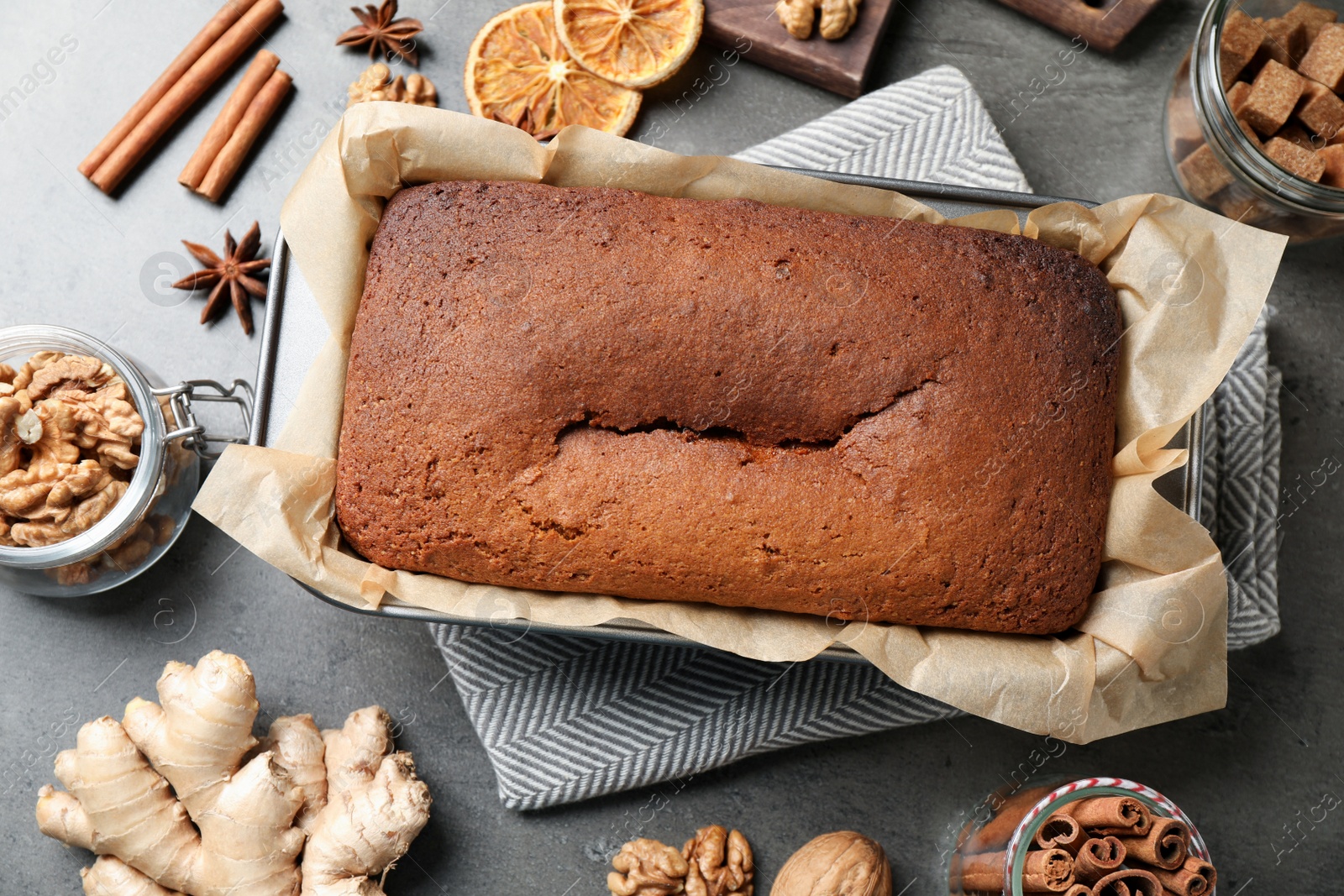 Photo of Flat lay composition with delicious gingerbread cake and ingredients on grey table