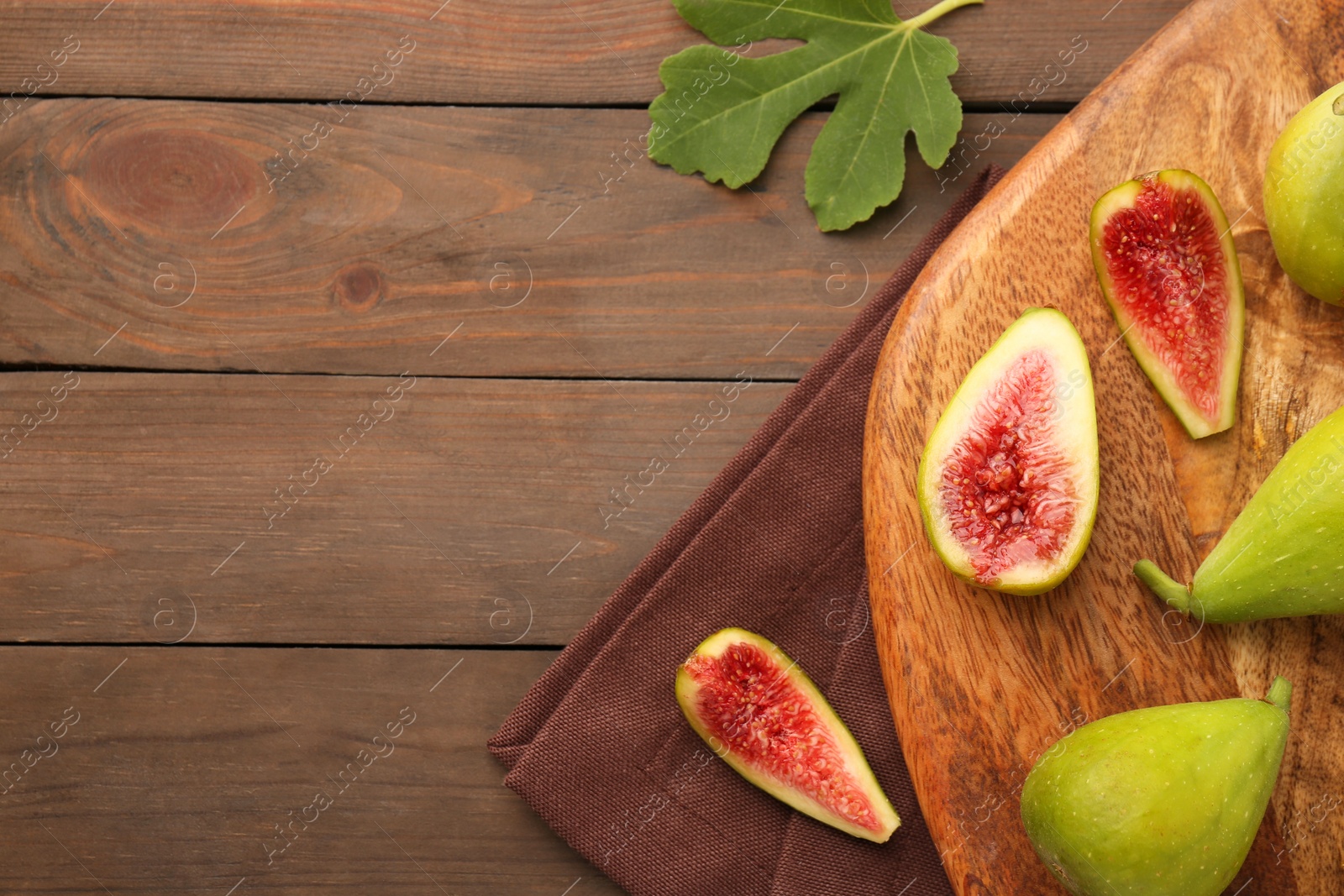 Photo of Cut and whole green figs on wooden table, flat lay. Space for text