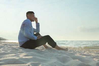 Photo of Happy businessman sitting on sandy beach. Business trip