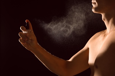 Young man spraying perfume on black background, closeup