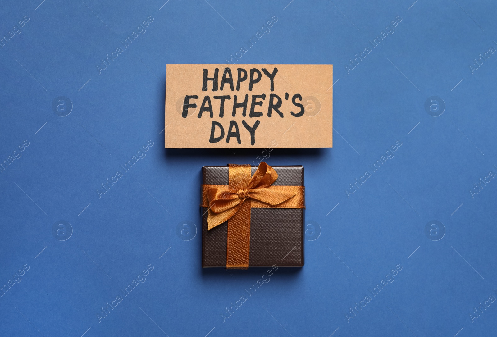 Photo of Card with phrase Happy Father's Day and gift box on blue background, flat lay