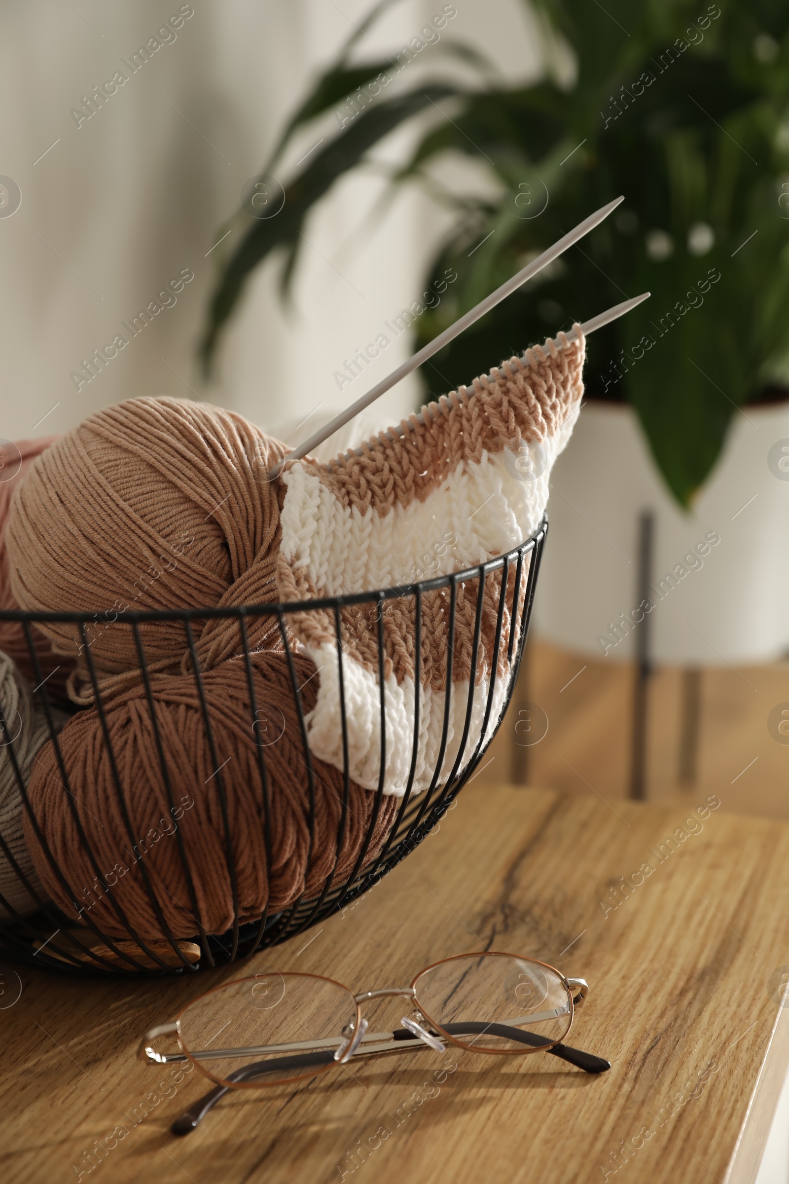 Photo of Glasses, yarn balls and knitting needles on wooden table indoors. Creative hobby