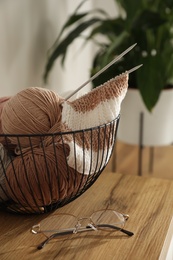 Glasses, yarn balls and knitting needles on wooden table indoors. Creative hobby