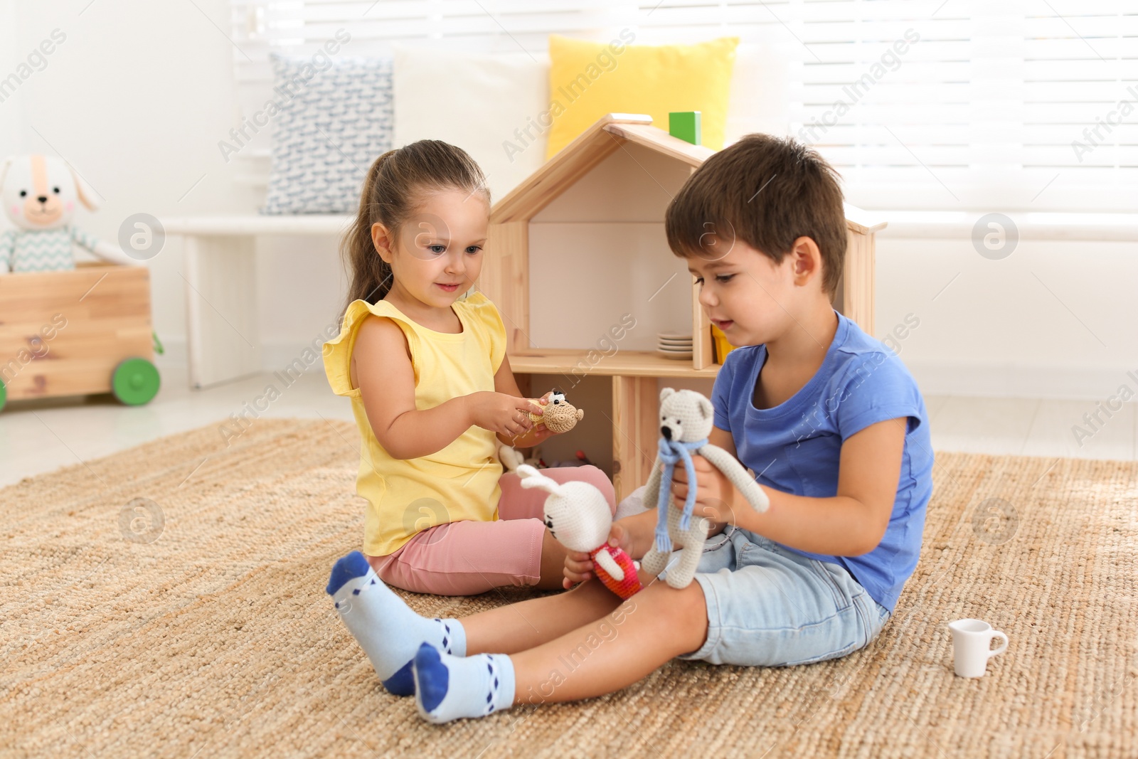 Photo of Cute little children playing with toys near wooden house on floor at home