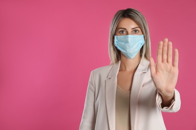Photo of Woman in protective mask showing stop gesture on pink background, space for text. Prevent spreading of coronavirus