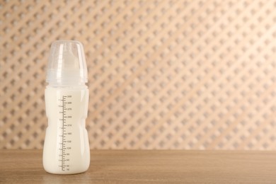 Feeding bottle with infant formula on wooden table, space for text. Baby milk