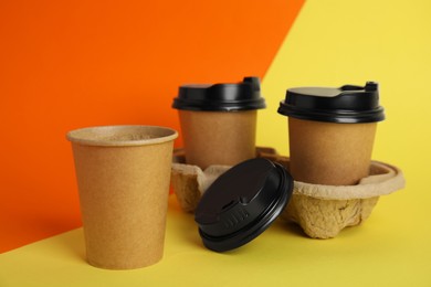 Takeaway paper coffee cups with plastic lids and cardboard holder on color background