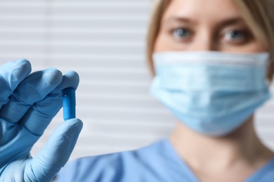 Doctor holding pill on light background, selective focus. Space for text