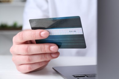 Online payment. Woman with laptop and credit card at white table, closeup