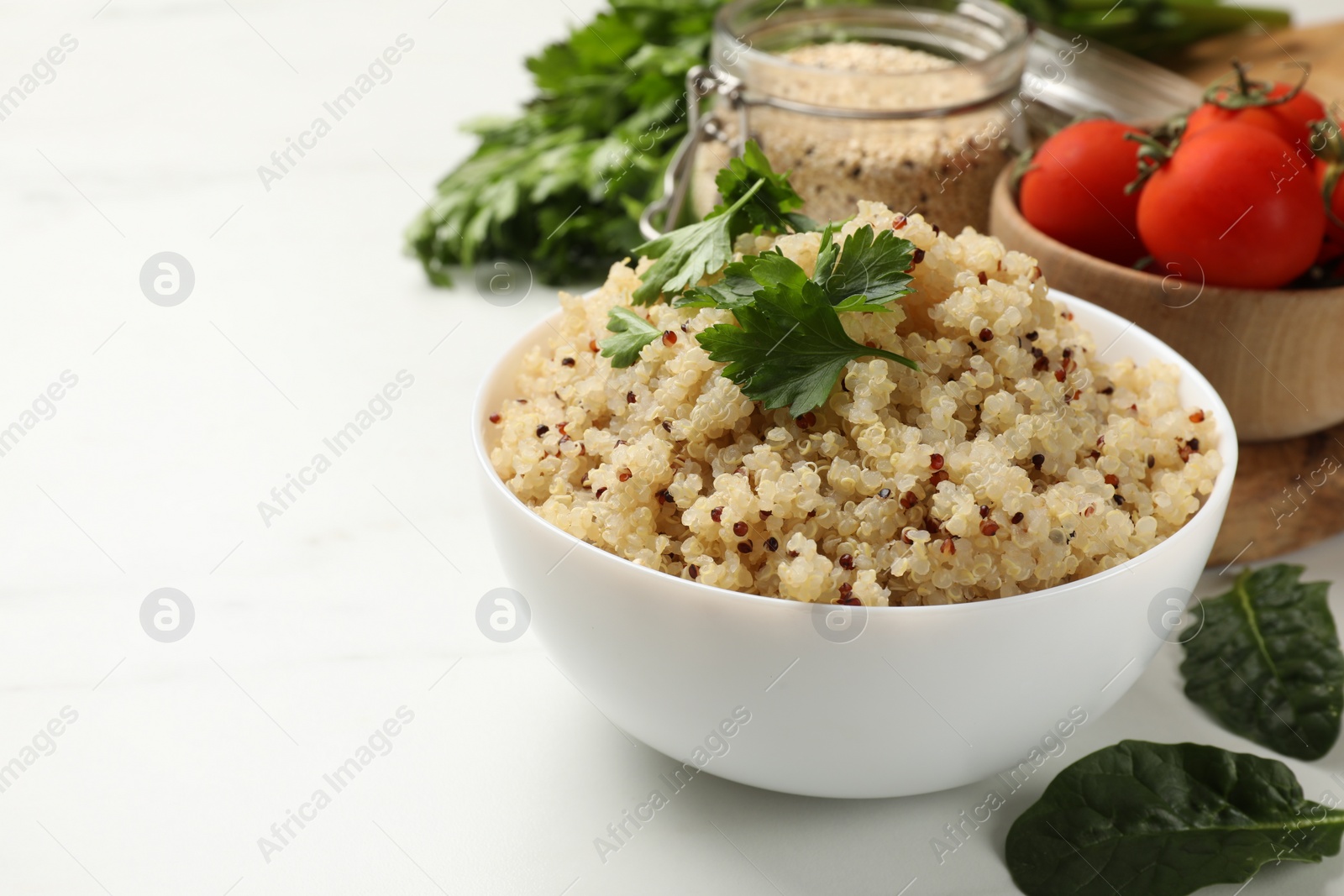 Photo of Tasty quinoa porridge with parsley in bowl on white table, closeup. Space for text